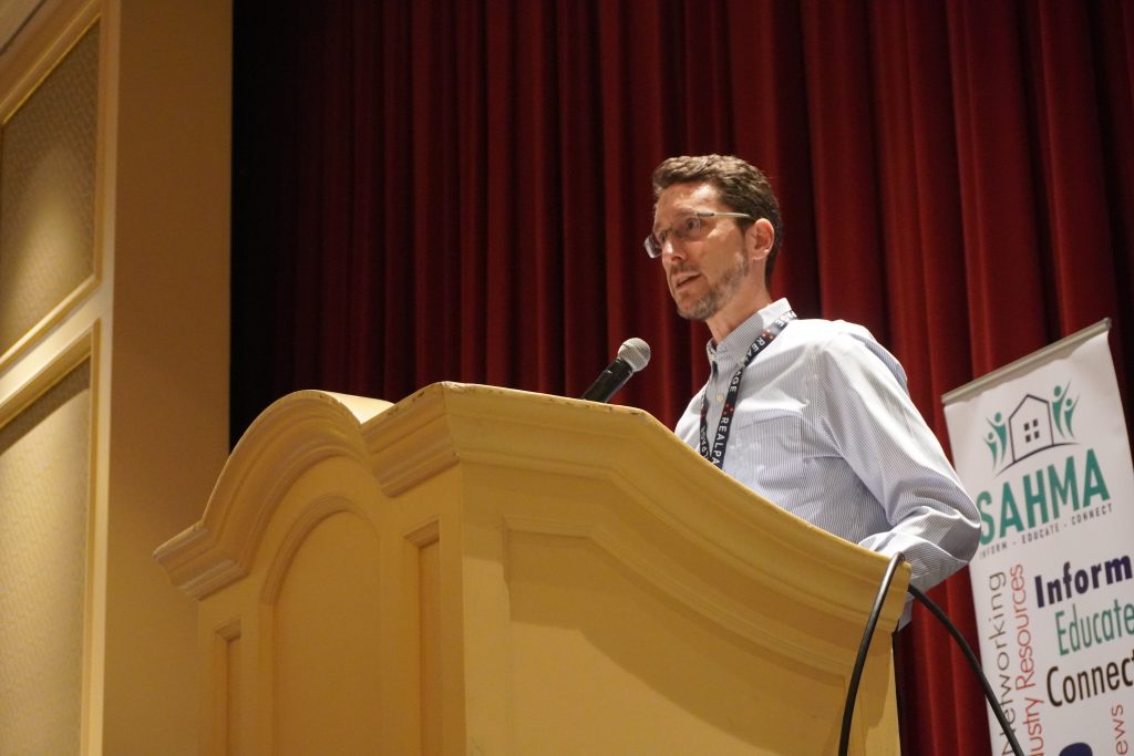 Speaker stands at a podium during a SAHMA conference presentation.