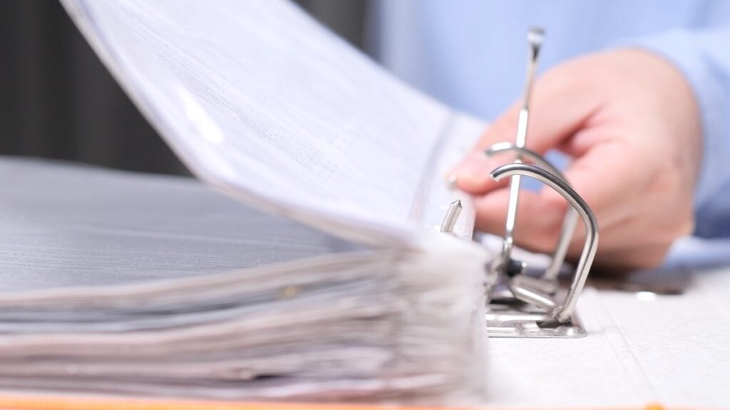 Close-up of a person reviewing documents in an open binder, representing HUD-assisted housing compliance, eligibility documentation, and program oversight, HUD OIG enforcement