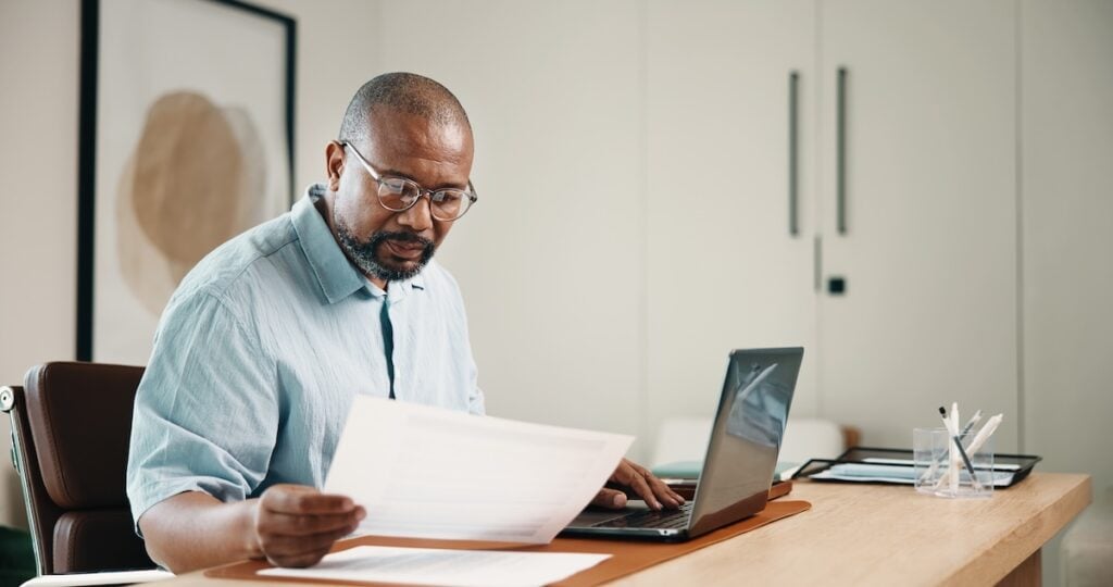 Man at a desk reviewing a printed document while working on a laptop in an office, MOR findings
